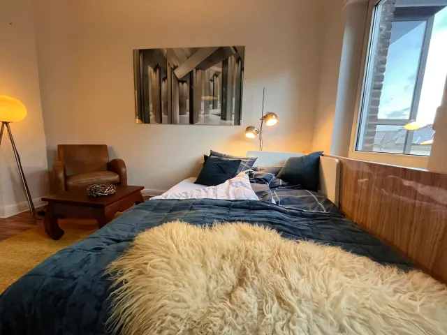 BookNoFees: Ferienwohnung in Mülheim An Der Ruhr – Schlafzimmer mit blauer Bettwäsche, Felldecke, Ledersessel und schrägem Fenster