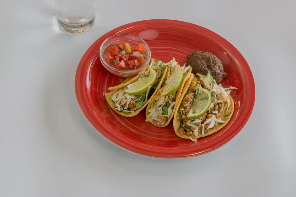 BookNoFees: Photo d’illustration : Trois tacos garnis de tranches de citron vert et de salsa, présentés sur une assiette rouge
