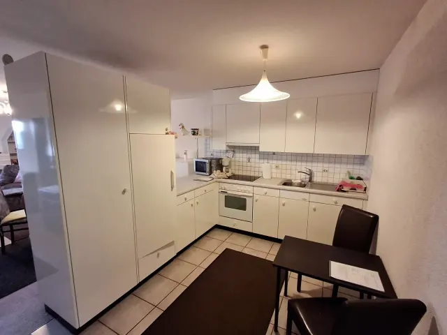 BookNoFees : location de vacances à Gailingen, Bade-Wurtemberg, Allemagne – Cuisine avec des placards blancs, une cuisinière, un évier, un micro-ondes et une petite table à manger avec des chaises