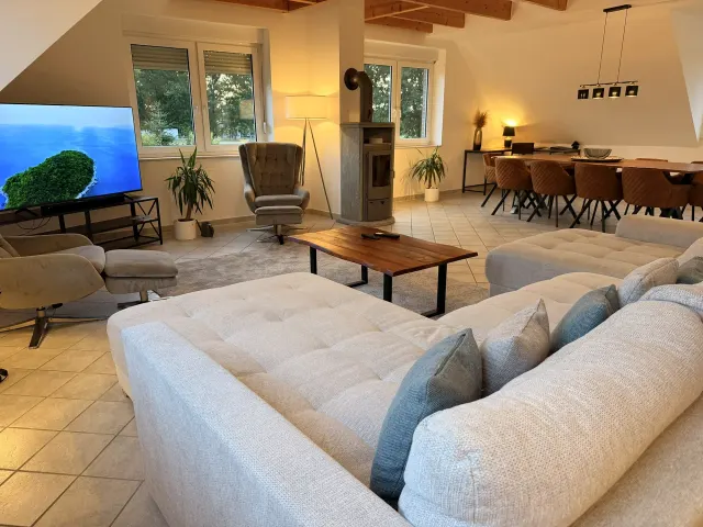BookNoFees : location de vacances à Stuhr – Salon avec canapé en L, poêle à bois et coin repas avec table en bois