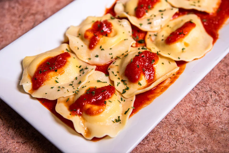Photo d’illustration : Raviolis nappés de sauce tomate et d'herbes aromatiques, présentés dans une assiette blanche